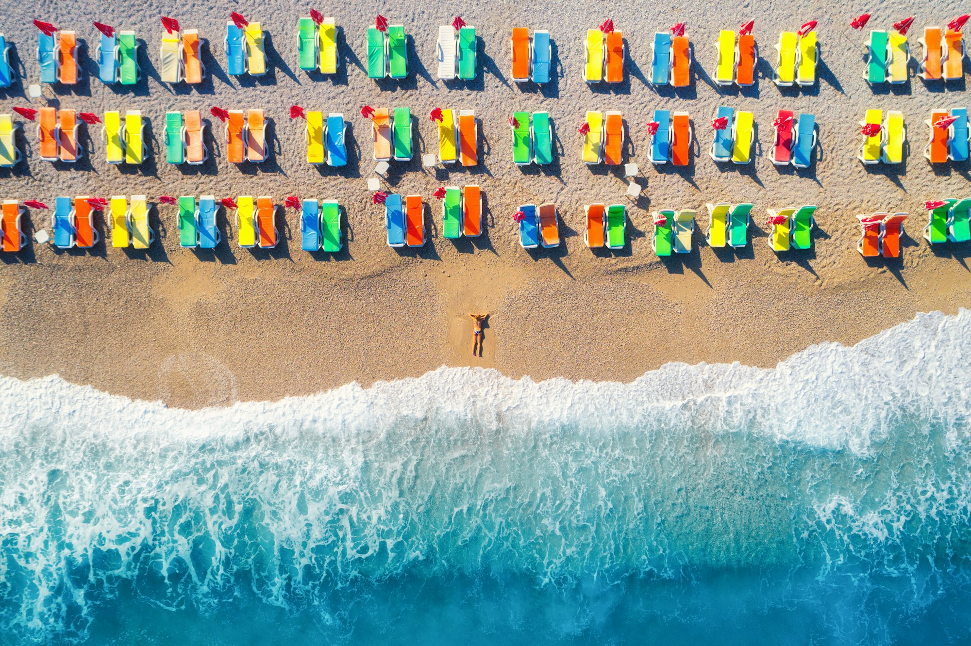 Aerial view of lying woman on the beach with colorful chaise-lounges